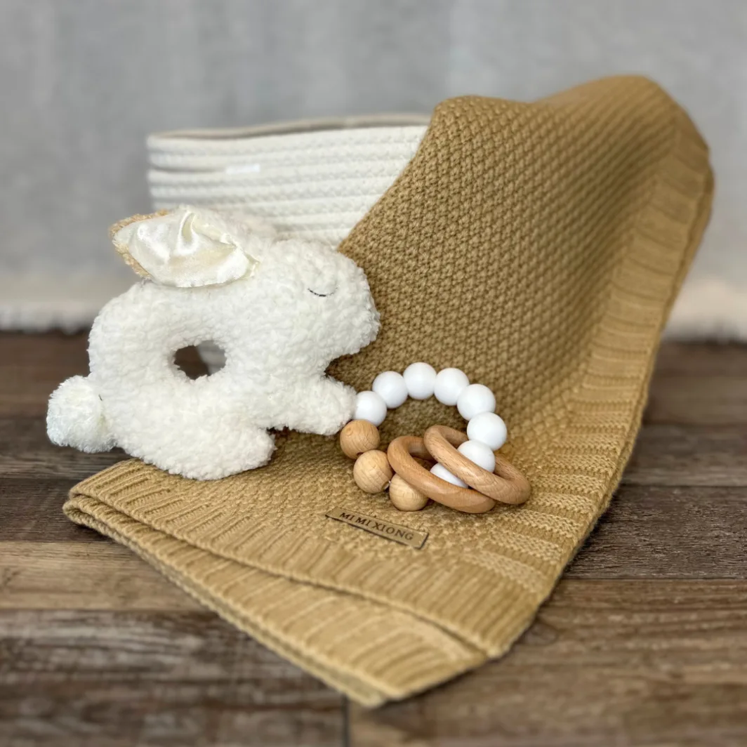 beautiful knit baby blanket, a white bunny rattle, and silver dumbell rattle