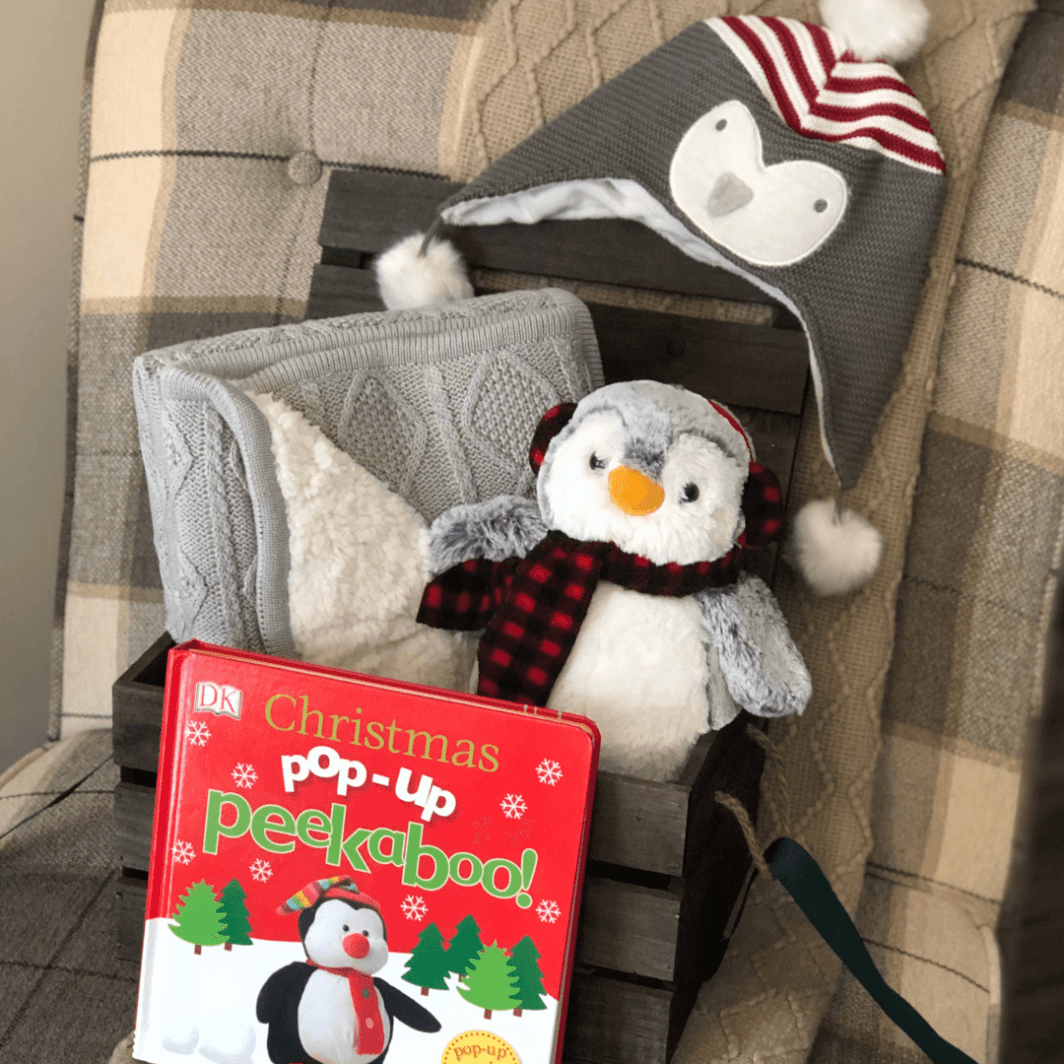 Wooden crate with a gorgeous fur backed gray knit baby blanket plush penguin toy penguin hat and christmas pop up book