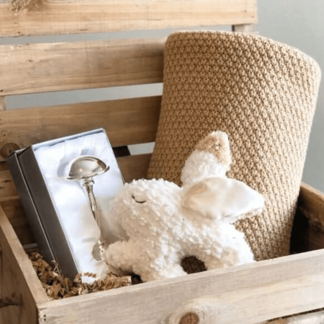 Wooden box with beautiful knit baby blanket, a white bunny rattle, and silver dumbell rattle