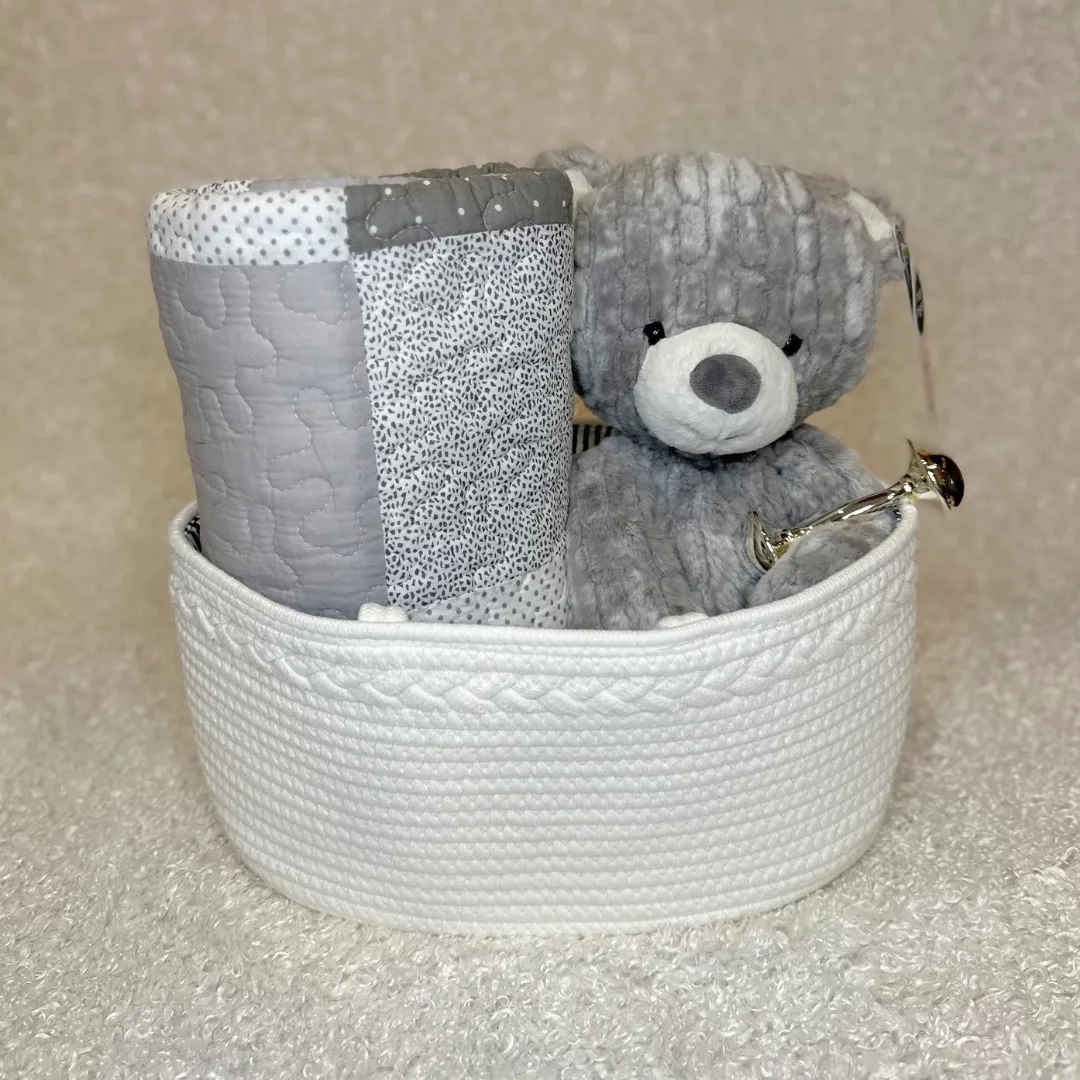 Gray quilt, gray mary meyer bear and rattle in a white basket